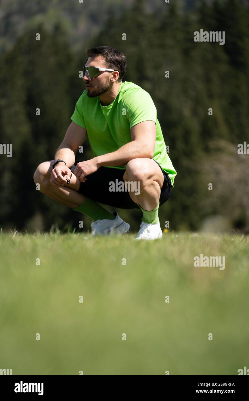 Ein Athlet hält an Einem hellen Tag auf dem Gras an, um sich von Einem anspruchsvollen Outdoor-Workout zu erholen, umgeben von Bäumen Stockfoto