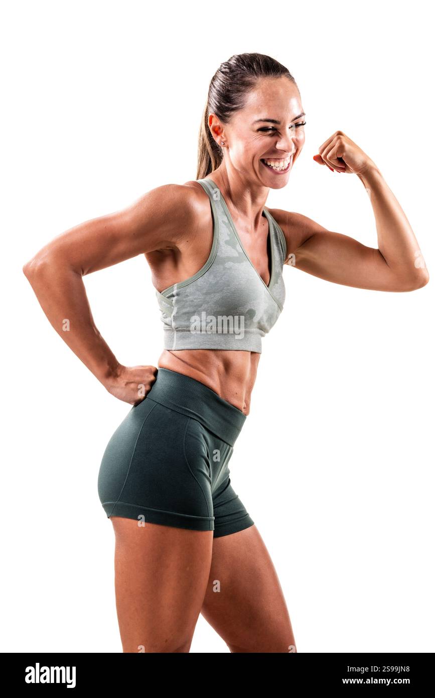 Eine fröhliche und fitte Frau posiert selbstbewusst, beugt ihre Arme, zeigt ihren fröhlichen Geist und ihr Engagement für Fitness, gekleidet in trendiger Sportkleidung Stockfoto