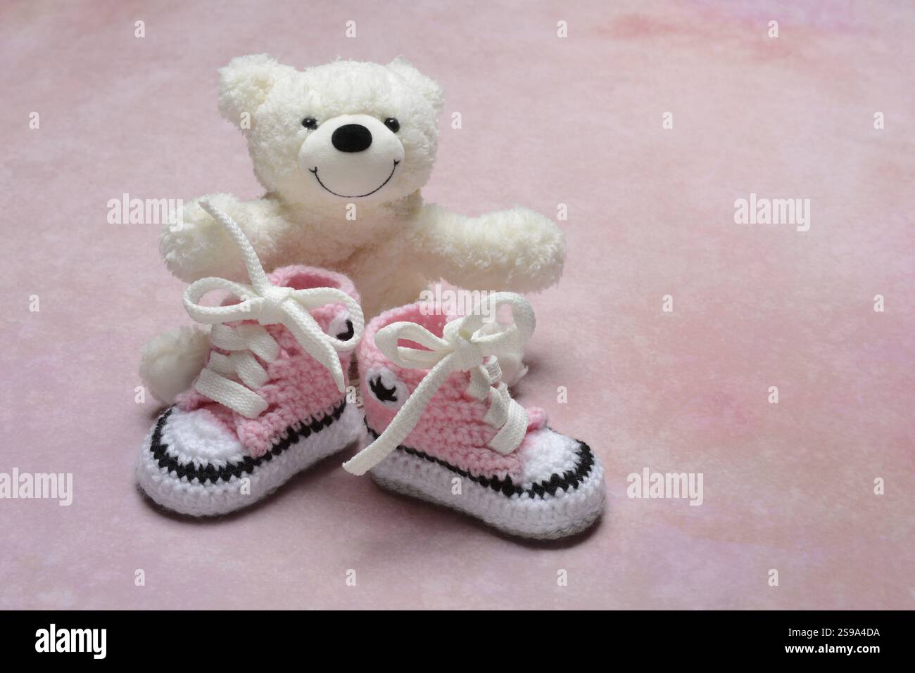 Pinkfarbene Babyschuhe mit Teddybär, rosa Hintergrund Stockfoto