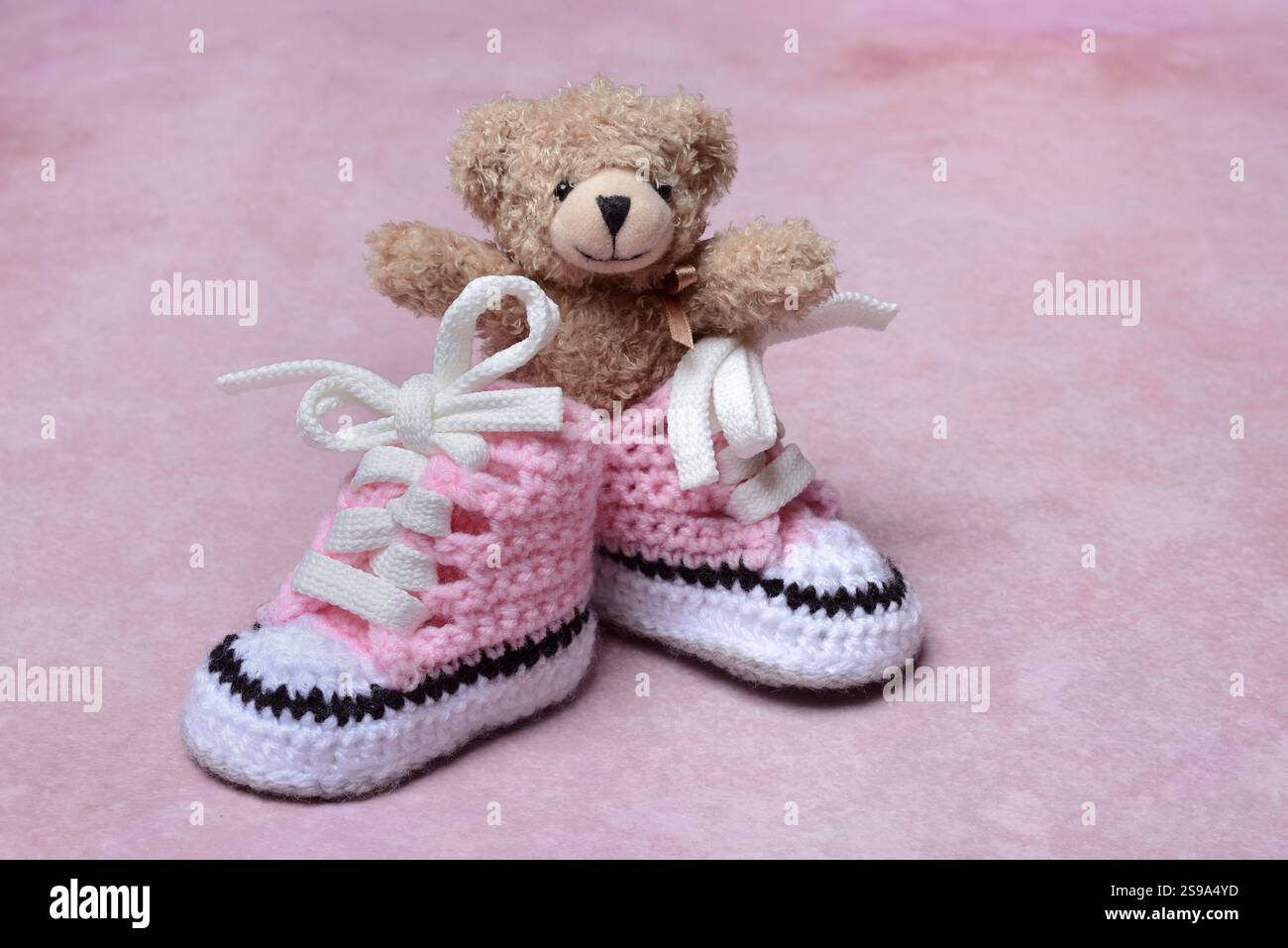 Babyschuhe und Teddybär mit rosa Hintergrund, handgefertigt Stockfoto