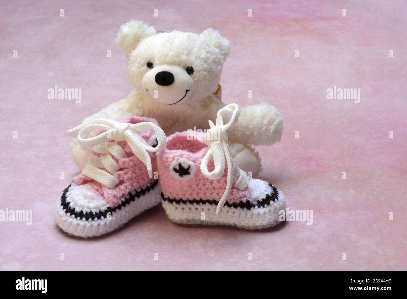 Pinkfarbene Babyschuhe mit Teddybär, rosa Hintergrund Stockfoto