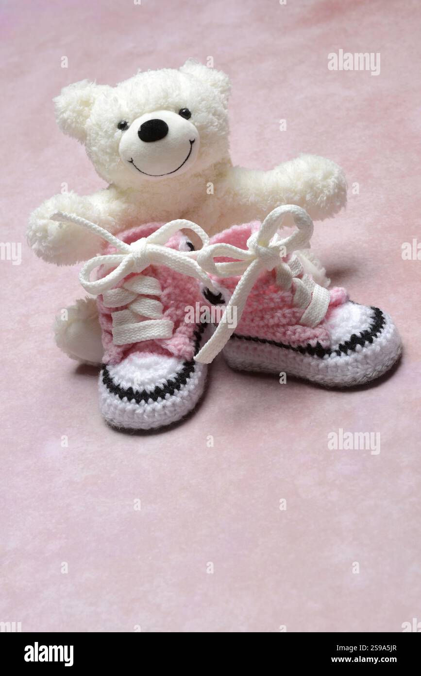 Pinkfarbene Babyschuhe mit Teddybär, rosa Hintergrund Stockfoto