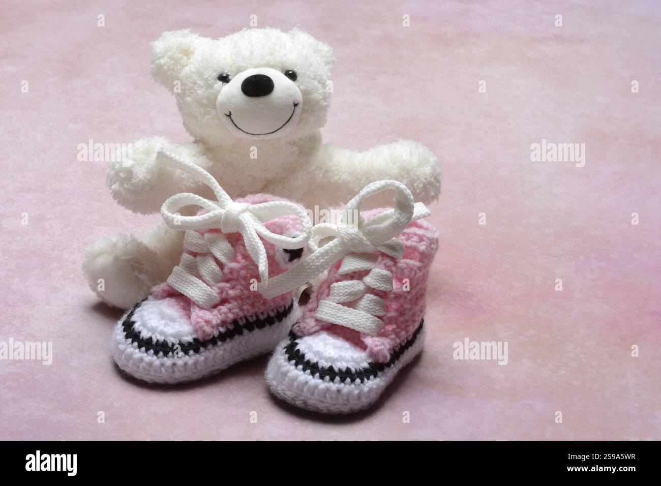 Pinkfarbene Babyschuhe mit Teddybär, rosa Hintergrund Stockfoto