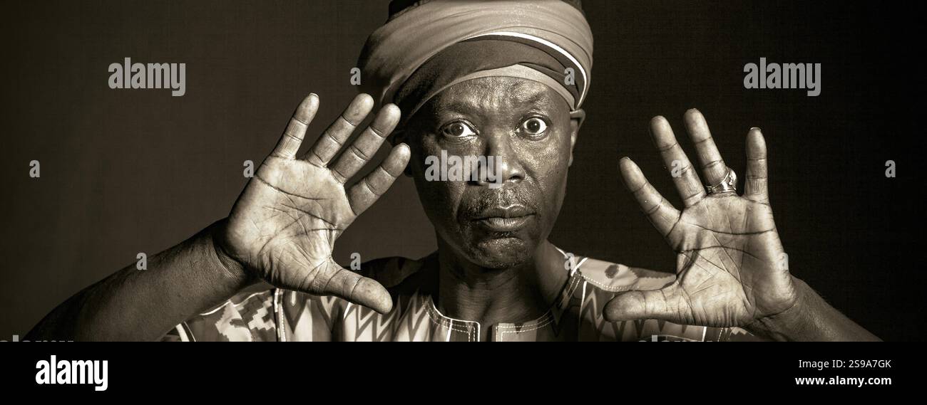 Afrikanischer Mann in traditioneller Kleidung, zahnloses Lächeln, auf grauem Hintergrund Stockfoto