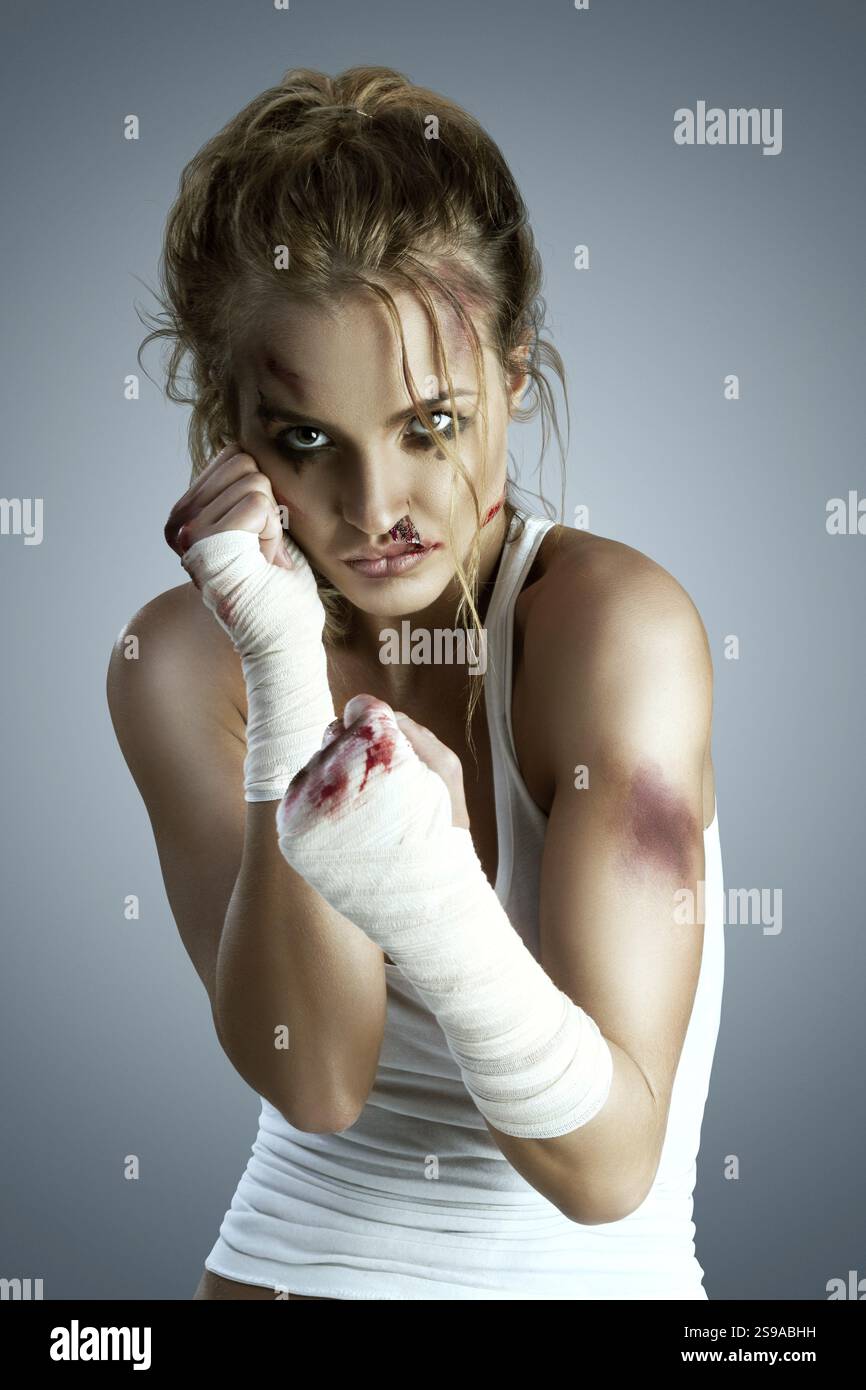 Aggressive Kämpferin mit blauen Flecken, eine blutige Bandage um ihre Fäuste, in einer Boxverteidigungsposition, bereit für den Kampf auf einer neutralen Stockfoto