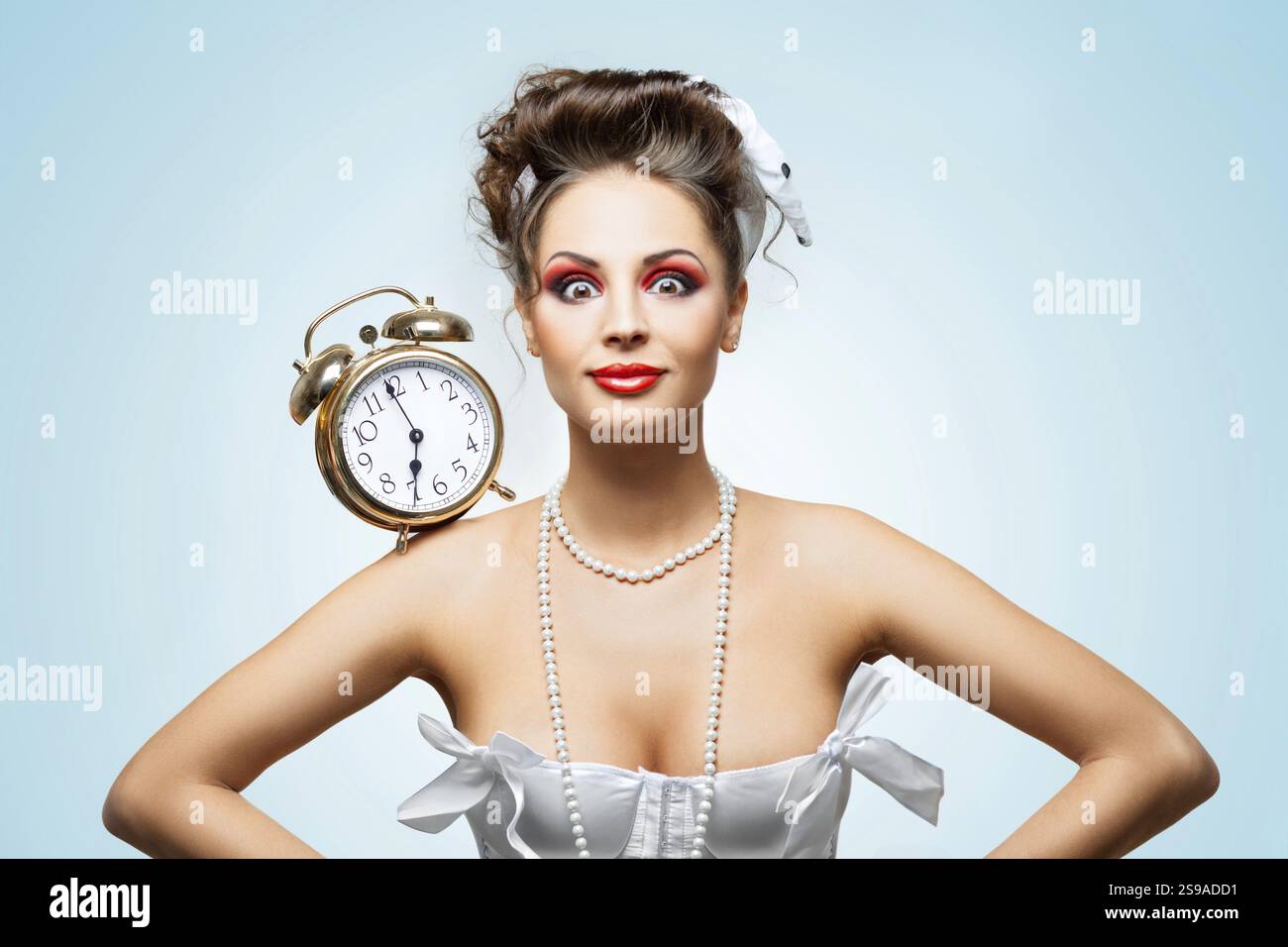 Ein wunderschönes Vintage-Mädchen in einem weißen Hochzeitskleid mit einem Retro-Wecker auf der Schulter am Morgen Stockfoto