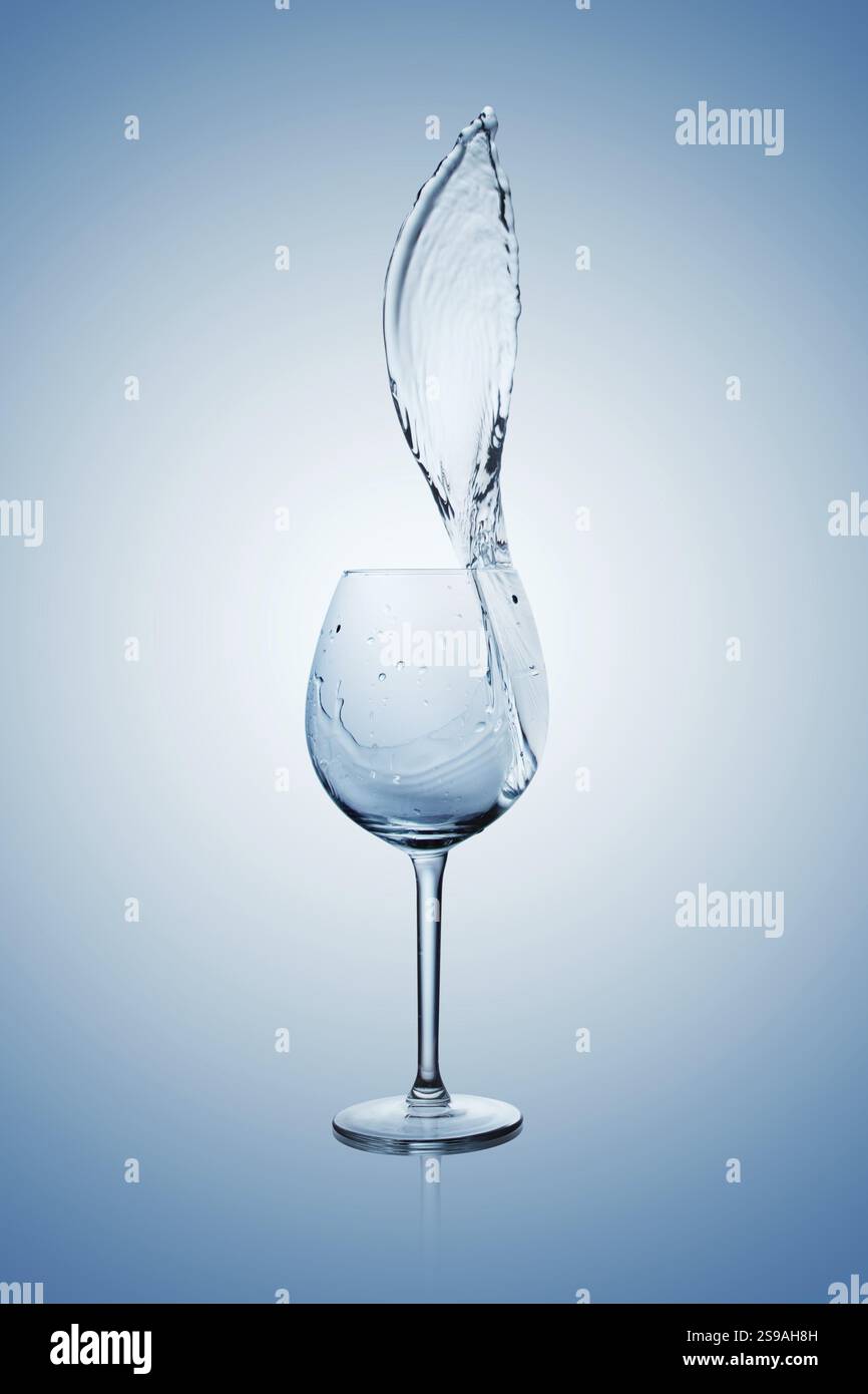 Wasser, das in ein Weinglas mit Stiel spritzt oder aus ihm austritt Stockfoto