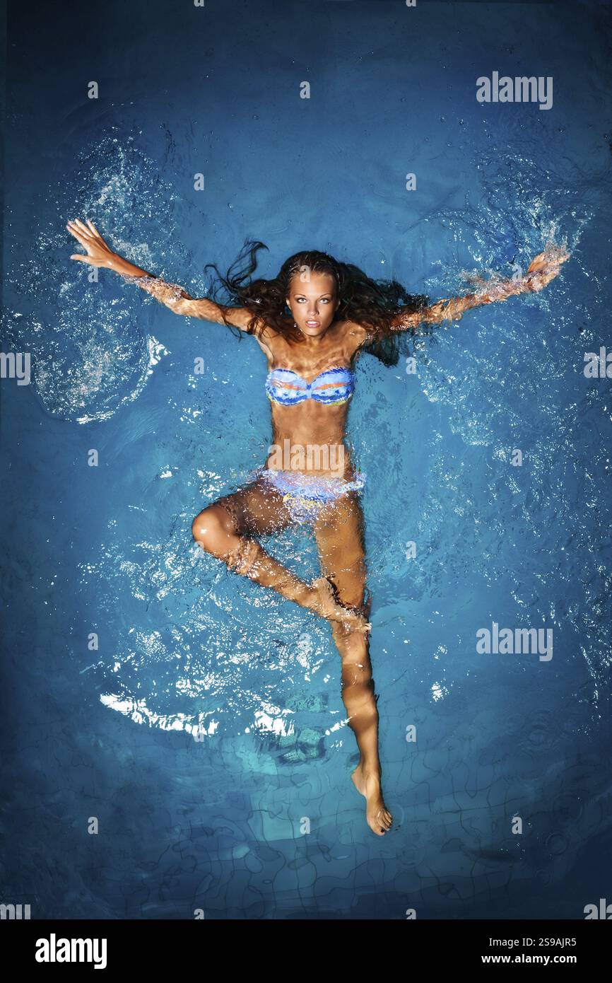 Eine sexy gebräunte Dame in einem farbenfrohen Bikini liegt in einem Swimmingpool Stockfoto