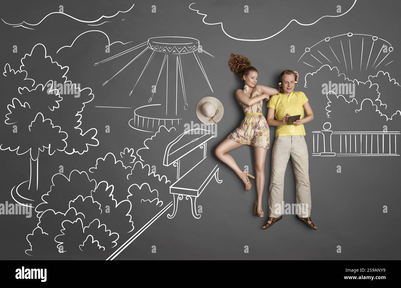 Liebesgeschichten-Konzept eines romantischen Paares vor Kreidezeichnungen-Hintergrund. Männlich, der Kopfhörer trägt und im Internet surft, weiblich versucht, anzuziehen Stockfoto