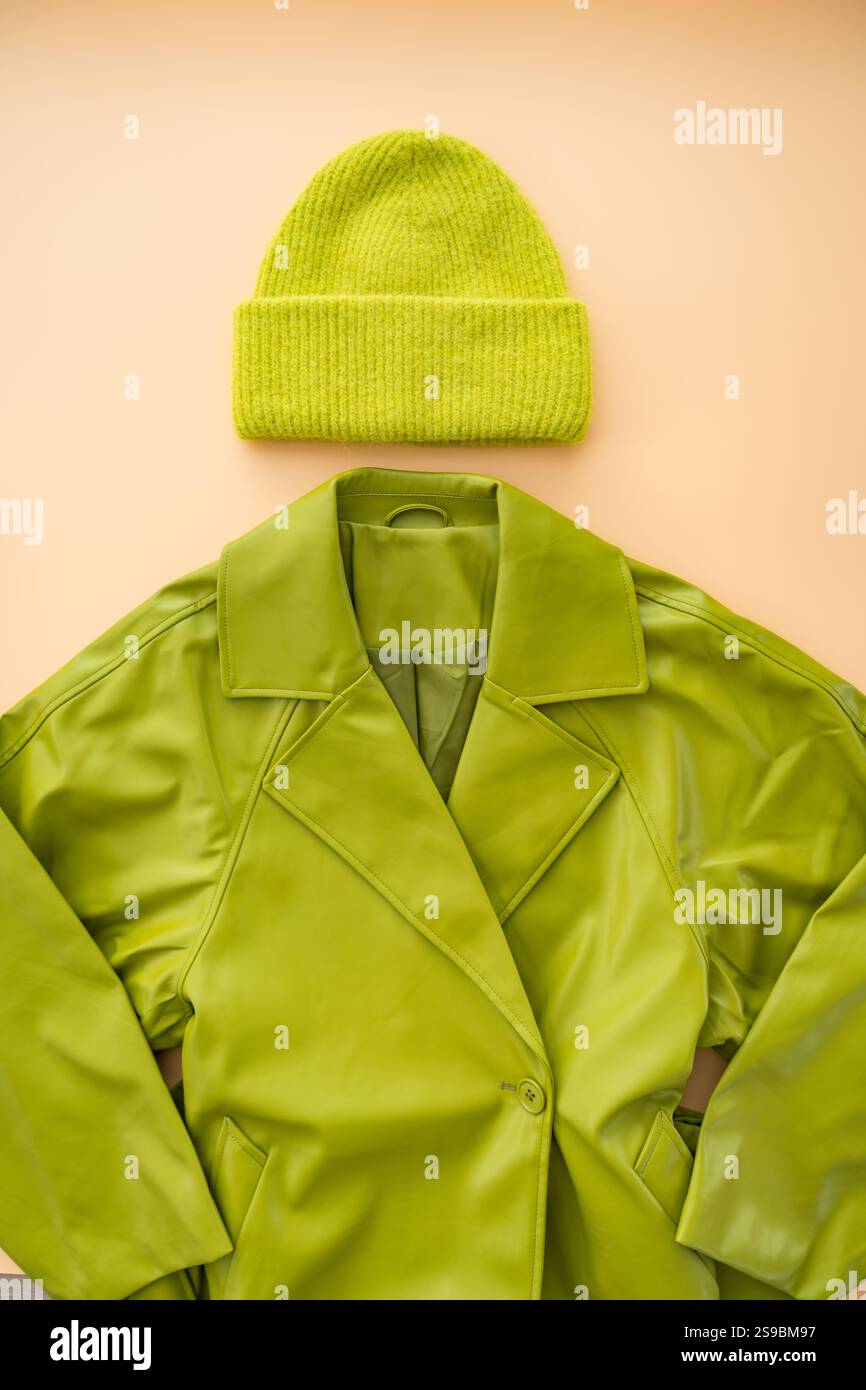 Flacher Lagen aus grünem Kunstledermantel, Kaschmirhut aus recycelten Materialien auf beigefarbenem Hintergrund. Stockfoto