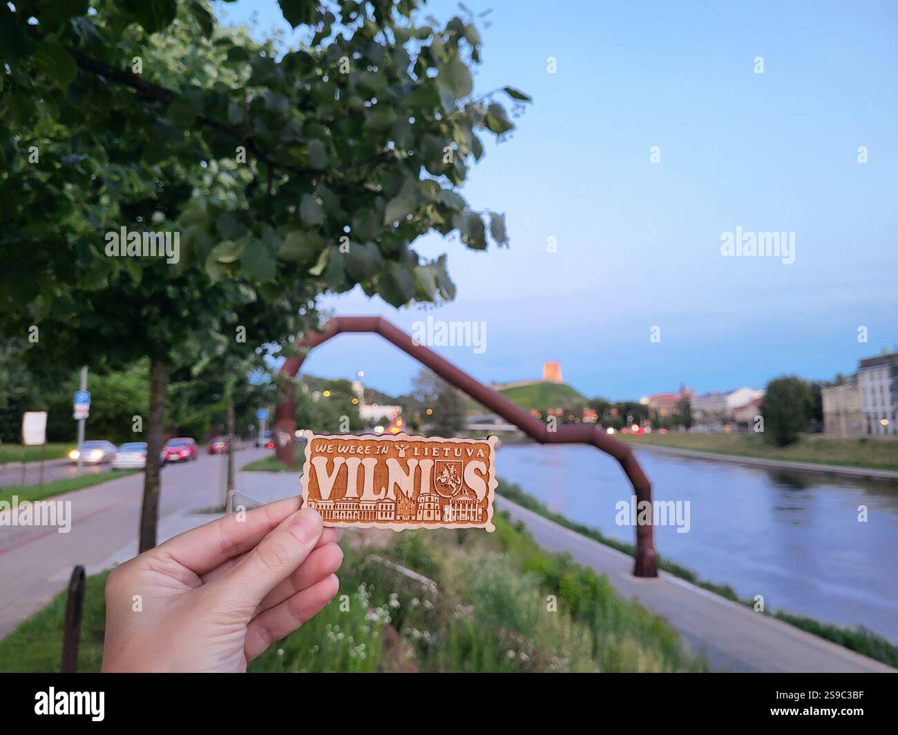 Vilnius, Litauen - 14-07-2022 - Eine Person hält einen hölzernen Souvenirmagnet für Touristen vor dem Hintergrund eines informellen Symbols der Stadt - Smartphone-aufgenommenes Stockfoto