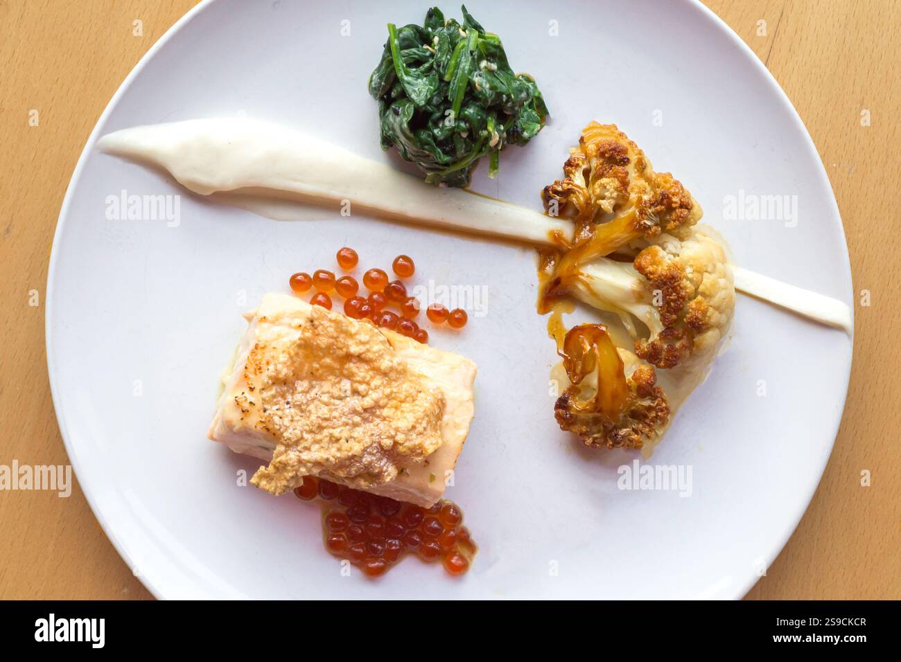 Gourmet-Gericht mit Lachs, Spinat, Blumenkohl und Reh auf eleganter weißer Platte Stockfoto