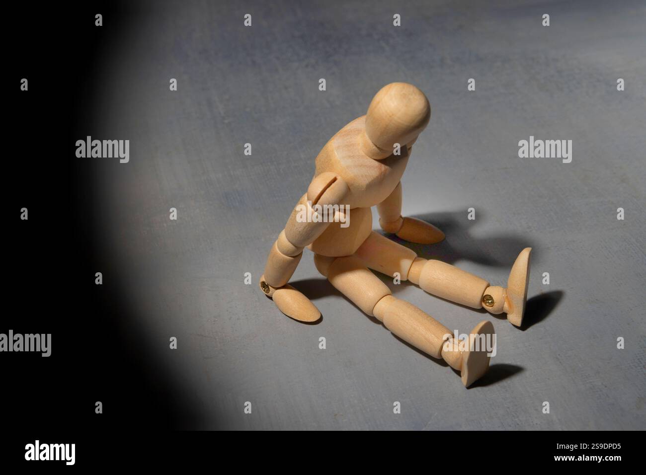 Eine hölzerne Schaufensterpuppe sitzt allein in der Dunkelheit und symbolisiert Einsamkeit, Isolation und Verzweiflung. Stockfoto