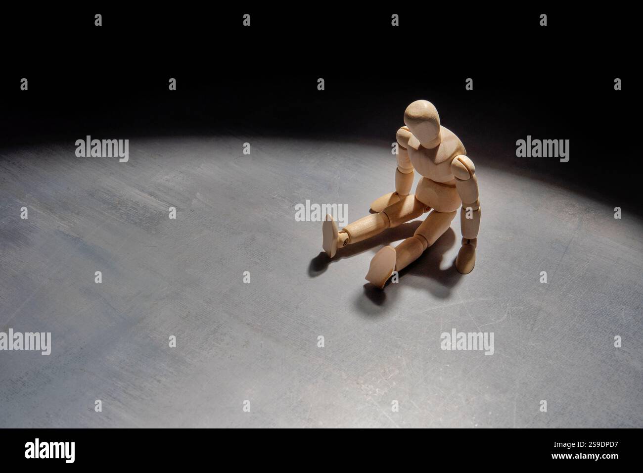 Eine hölzerne Schaufensterpuppe sitzt allein in der Dunkelheit und symbolisiert Einsamkeit, Isolation und Verzweiflung. Stockfoto