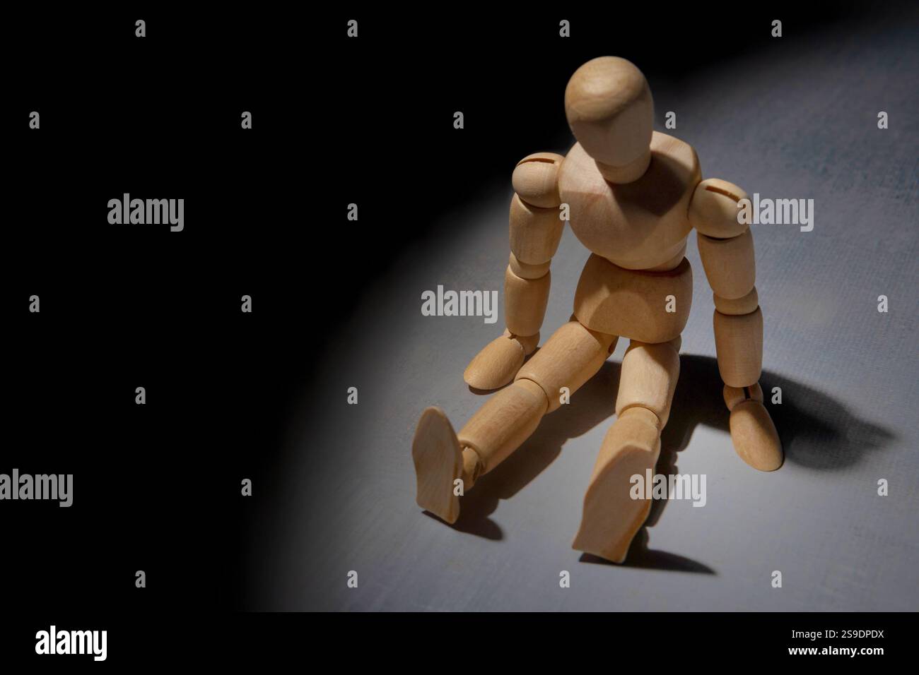 Eine hölzerne Schaufensterpuppe sitzt allein in der Dunkelheit und symbolisiert Einsamkeit, Isolation und Verzweiflung. Stockfoto