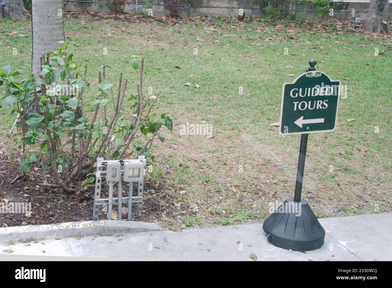 Grünes Schild für geführte Tour auf einem Ständer mit einem Pfeil nach links. Auf einem Gehweg mit grünem Gras und Pflanzen. Keine Leute und Platz zum Kopieren. Stockfoto