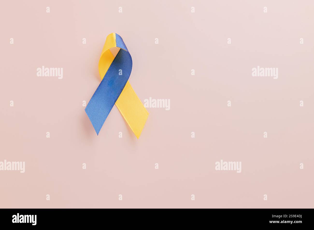 Welt-Down-Syndrom-Tag und Autismus-Bewusstsein mit globaler Unterstützung. Ein gelb-blaues Band auf rosafarbenem Hintergrund symbolisiert das Down-Syndrom Stockfoto