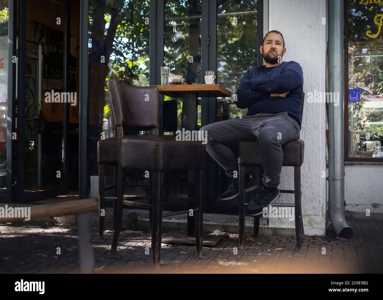 Belgrad, 17. September 2024: Ein Mann sitzt auf einem Hochstuhl vor einem Café mit kontemplativem Ausdruck. Stockfoto