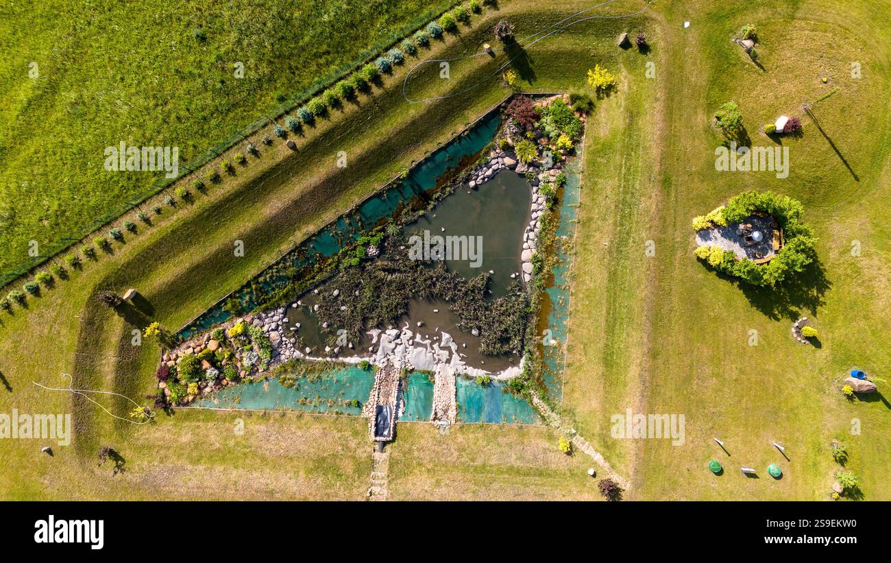 Blick aus der Vogelperspektive auf einen dreieckigen Teich, umgeben von grünem Gras und Landschaftsgärten. Stockfoto