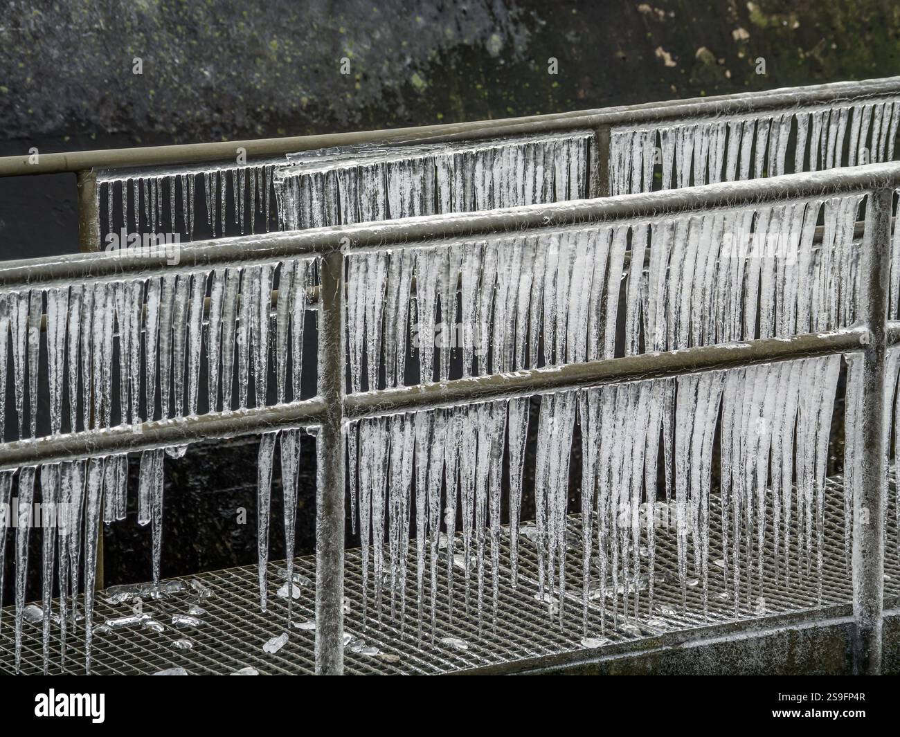 Eiszapfen formten sich entlang eines Stahlgeländers aufgrund des kalten Wetters und symbolisieren die raue Schönheit des Winters. Stockfoto