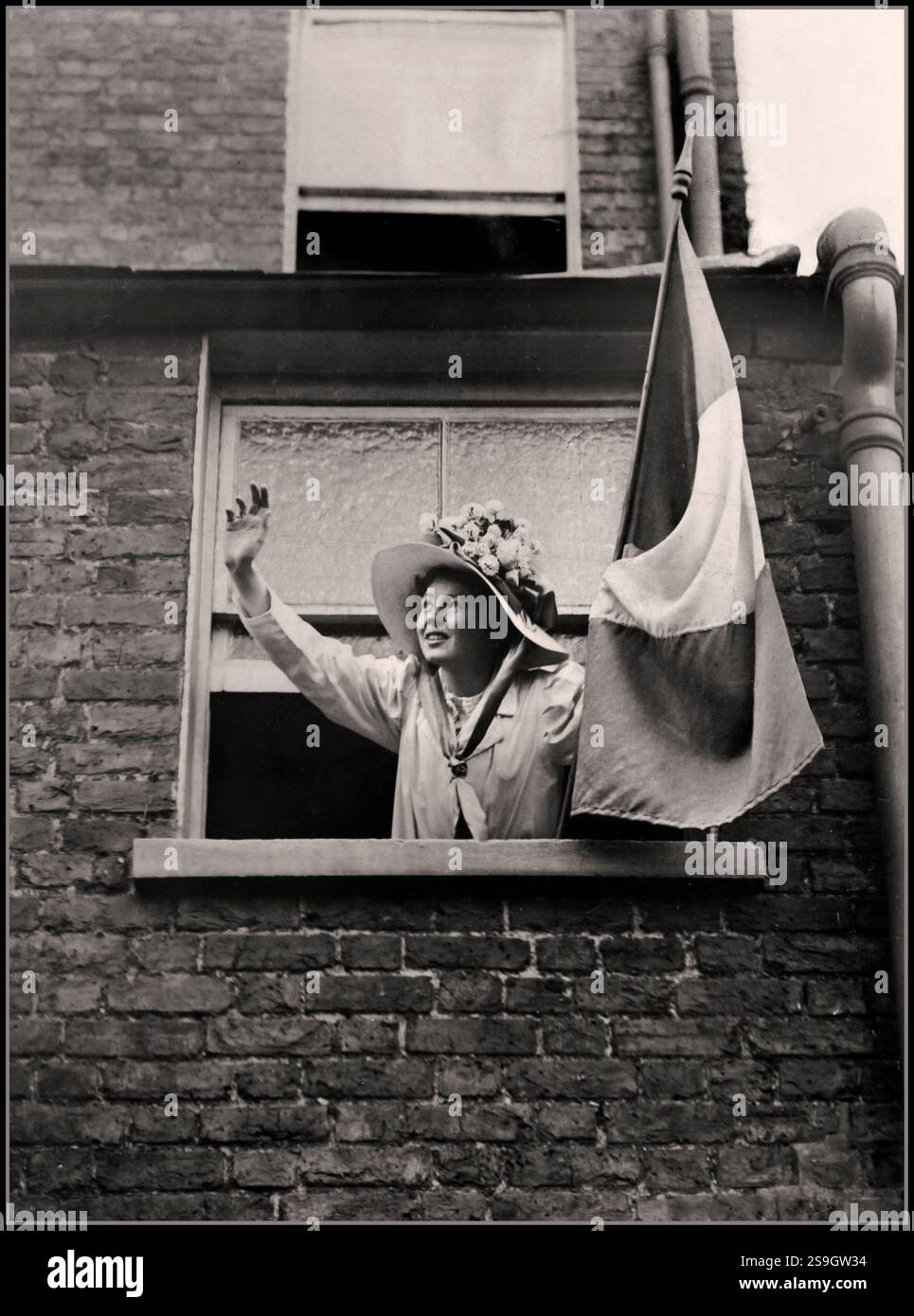 Christabel Pankhurst, die eine WSPU-Flagge (Women's Social & Political Union) hielt und aus dem Fenster eines Hauses winkte; 1900er Jahre Großbritannien Christabel Harriette Pankhurst (* 22. September 1880 – 13. Februar 1958) war eine britische Suffragette in Manchester. Sie war Mitbegründerin der Women's Social & Political Union (WSPU) und leitete ihre militanten Aktionen vom französischen Exil aus von 1912 bis 1913. Stockfoto