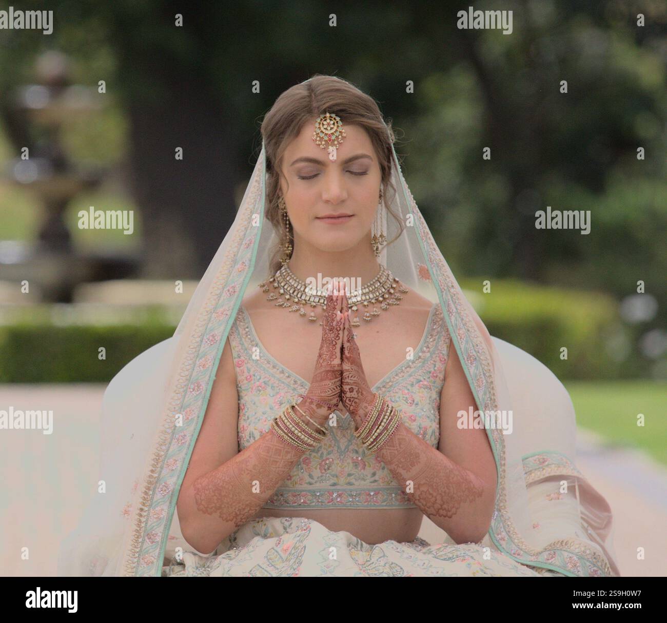 Atemberaubende kaukasische Braut in indischem Brautkleid im Gebet mit gefalteten Händen für ihre hinduistische Hochzeitszeremonie Stockfoto