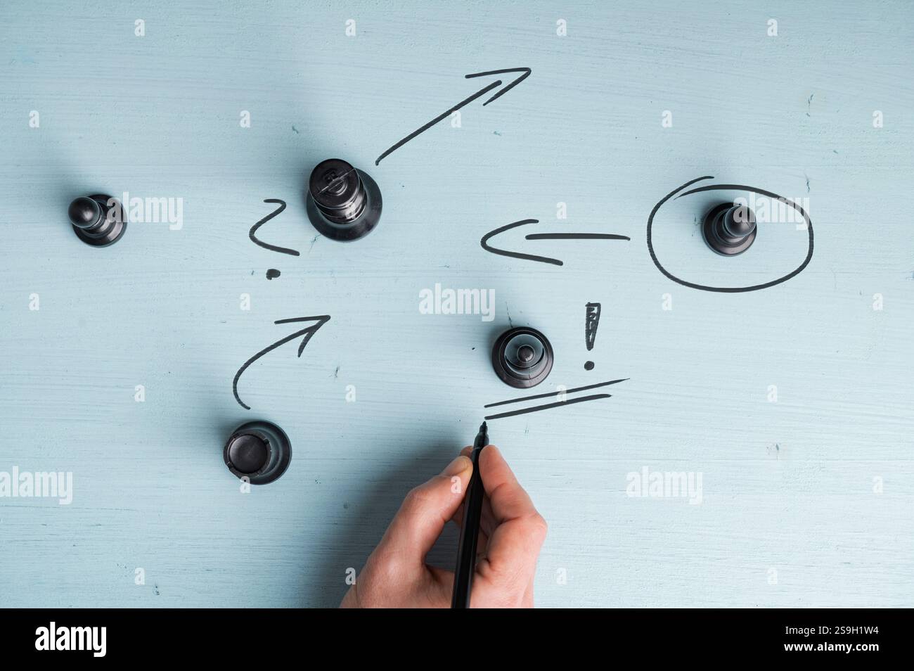 Eine Hand zeichnet Pfeile und Symbole um Schachfiguren auf einer blauen Oberfläche, die Strategie und Planung eines Unternehmens oder Startups veranschaulichen. Stockfoto