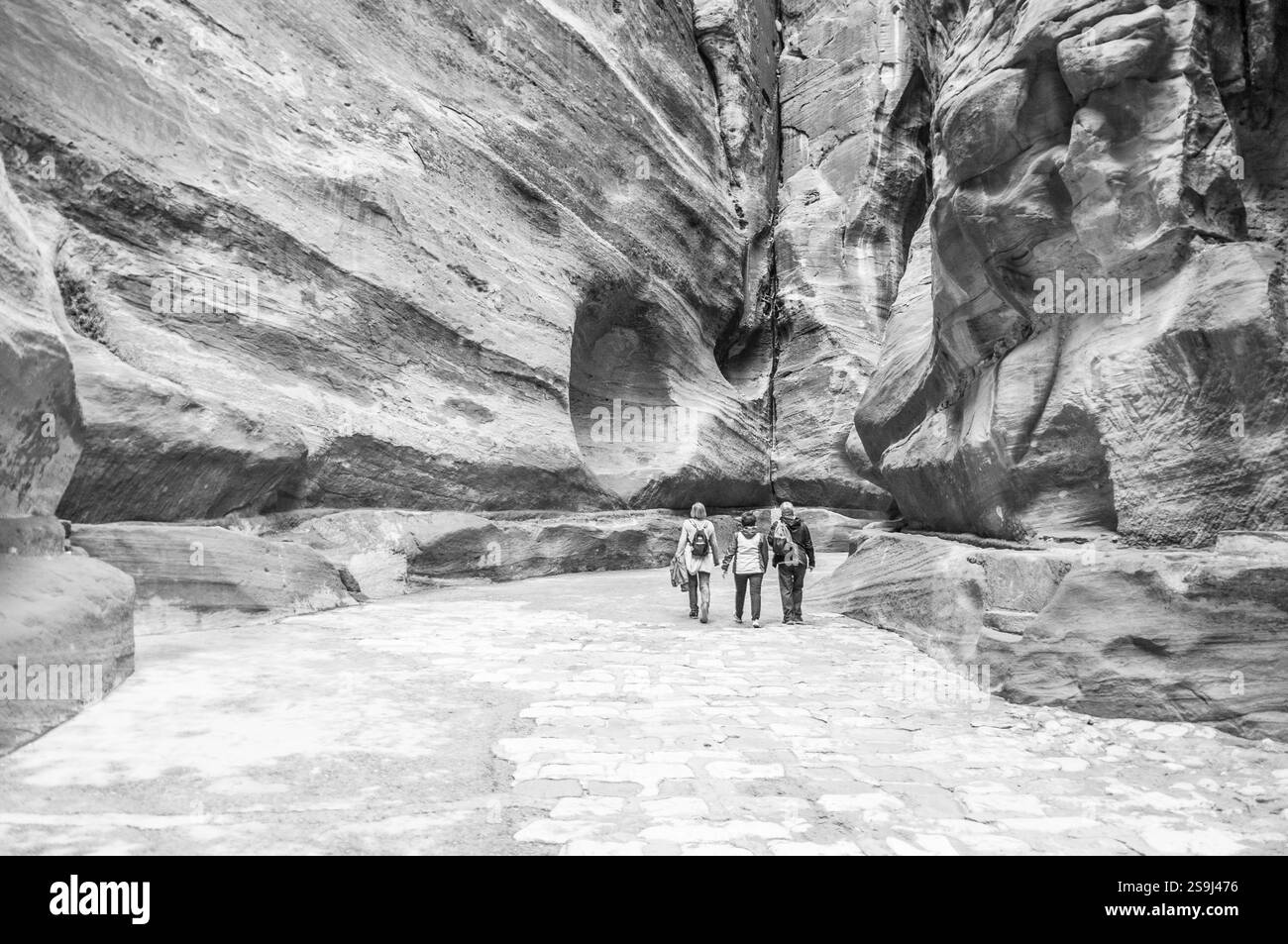 Drei Personen laufen einen Weg entlang in einem felsigen Gebiet. Der Weg ist schmal und kurvig, mit großen Felsen und Felsbrocken an den Seiten. Stockfoto
