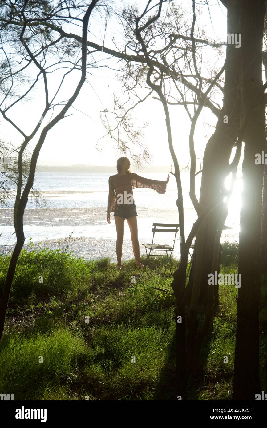 Silhouette einer jungen Frau in einem Wald am See. Es ist ein Spätsommernachmittag und das Sonnenlicht filtert durch die Bäume. Stockfoto