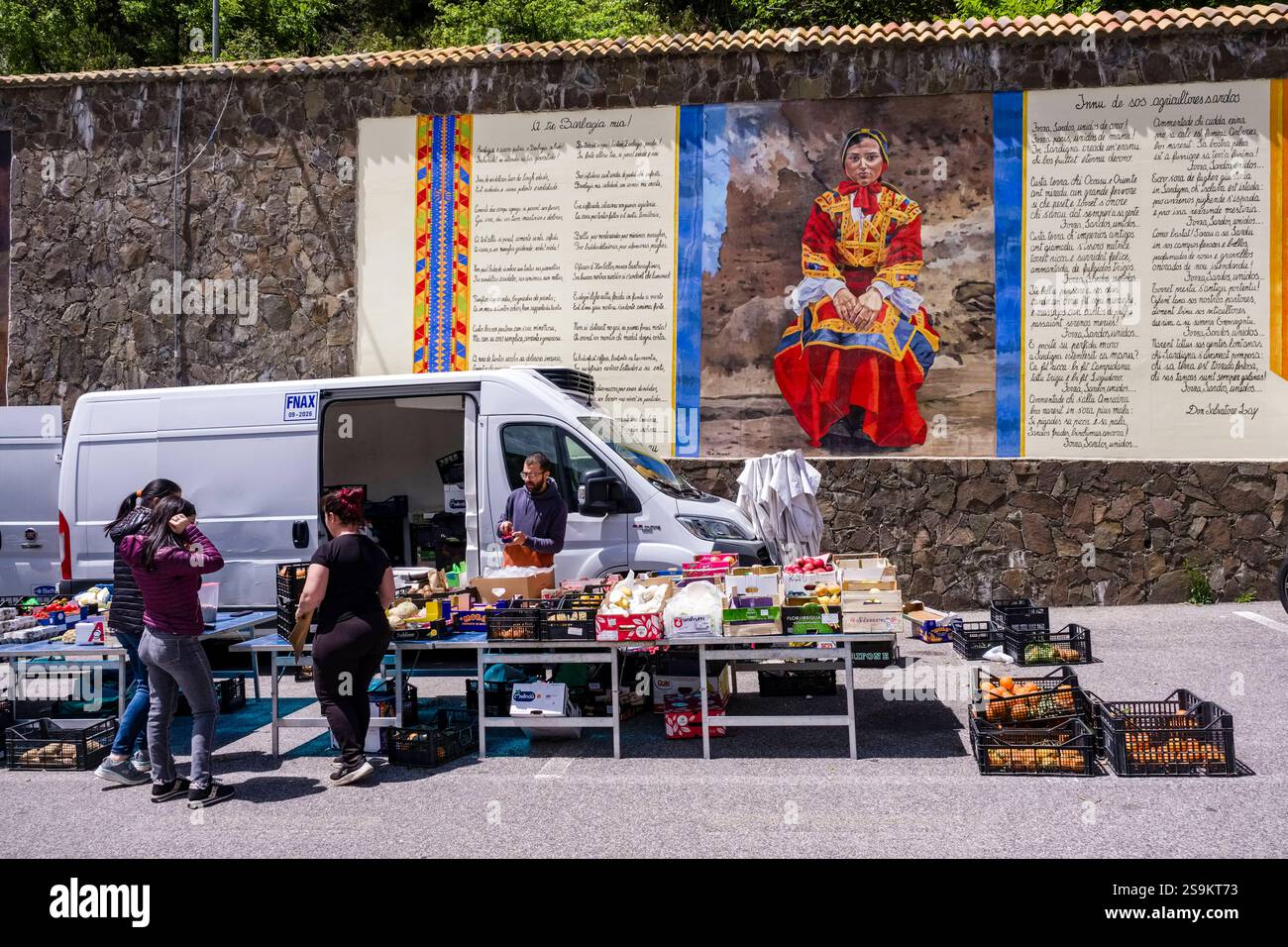 Wöchentlicher Obst- und Gemüsemarkt in der Stadt Desulo, mit einem großen farbenfrohen Gemälde einer Frau in traditioneller sardischer Kleidung an der Wand hinter mir Stockfoto