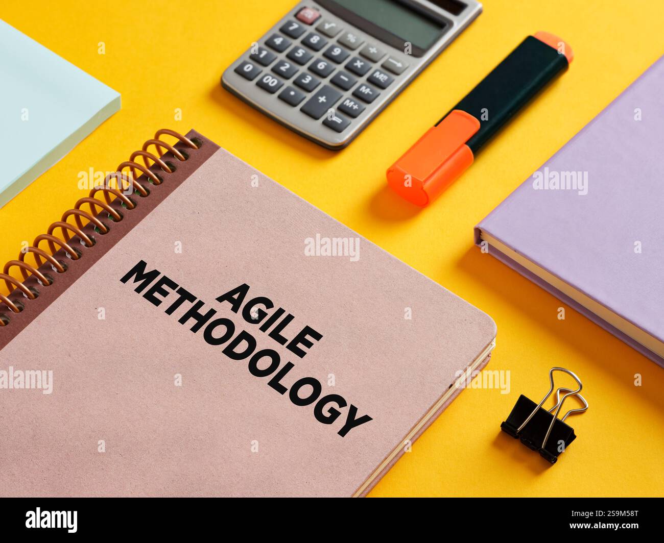 Notizbuch mit agiler Methodik auf dem Cover, begleitet von Rechner, Textmarker, Binderclip und Haftnotizen, die das Projektmanagement c verkörpern Stockfoto