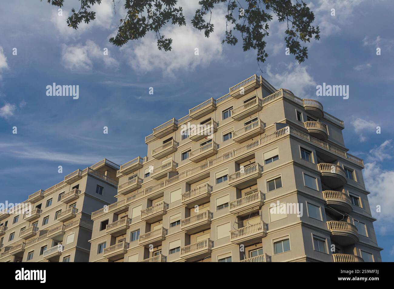Ein modernes Wohngebäude erhebt sich vor einem hellblauen Himmel in Albanien mit einzigartigen Balkonen und einem ansprechenden architektonischen Design, das von en eingerahmt wird Stockfoto