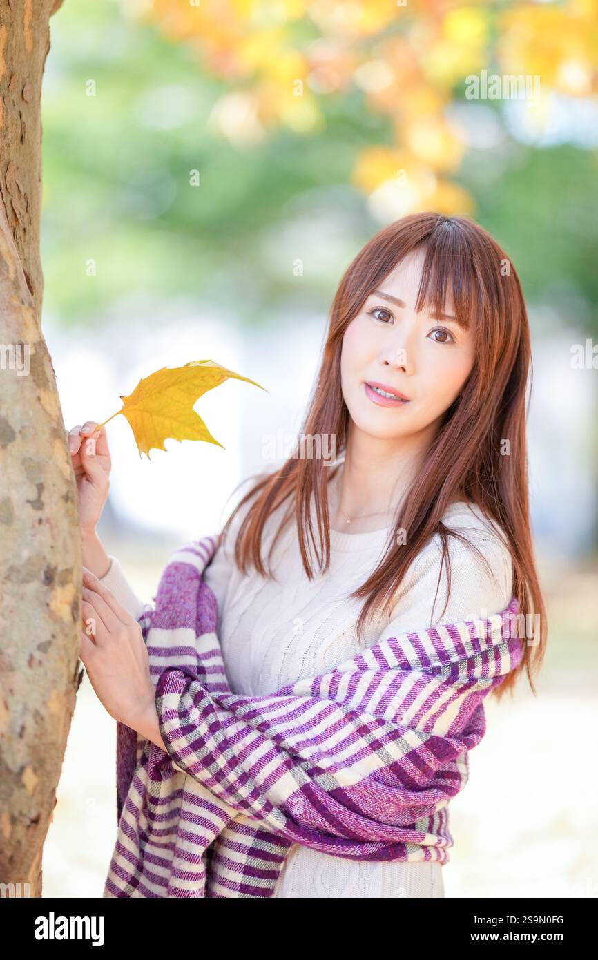 Eine Frau mit langen Haaren in ihren dreißiger Jahren steht in einem schönen Herbstlaub in einem schönen Herbstlaub. Stockfoto