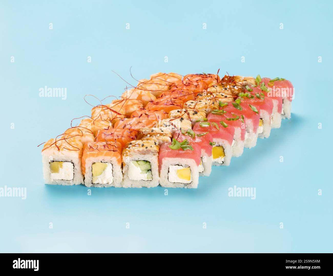 Philadelphia Roll Set mit Mango, Gurke und Avocado, gewickelt mit perfekt gewürztem Sushi-Reis und frischem Lachs, Thunfisch, Garnelen und geräuchertem Aal, dekorierten Chili-Garnen. Isoliert auf hellblauem Hintergrund Stockfoto