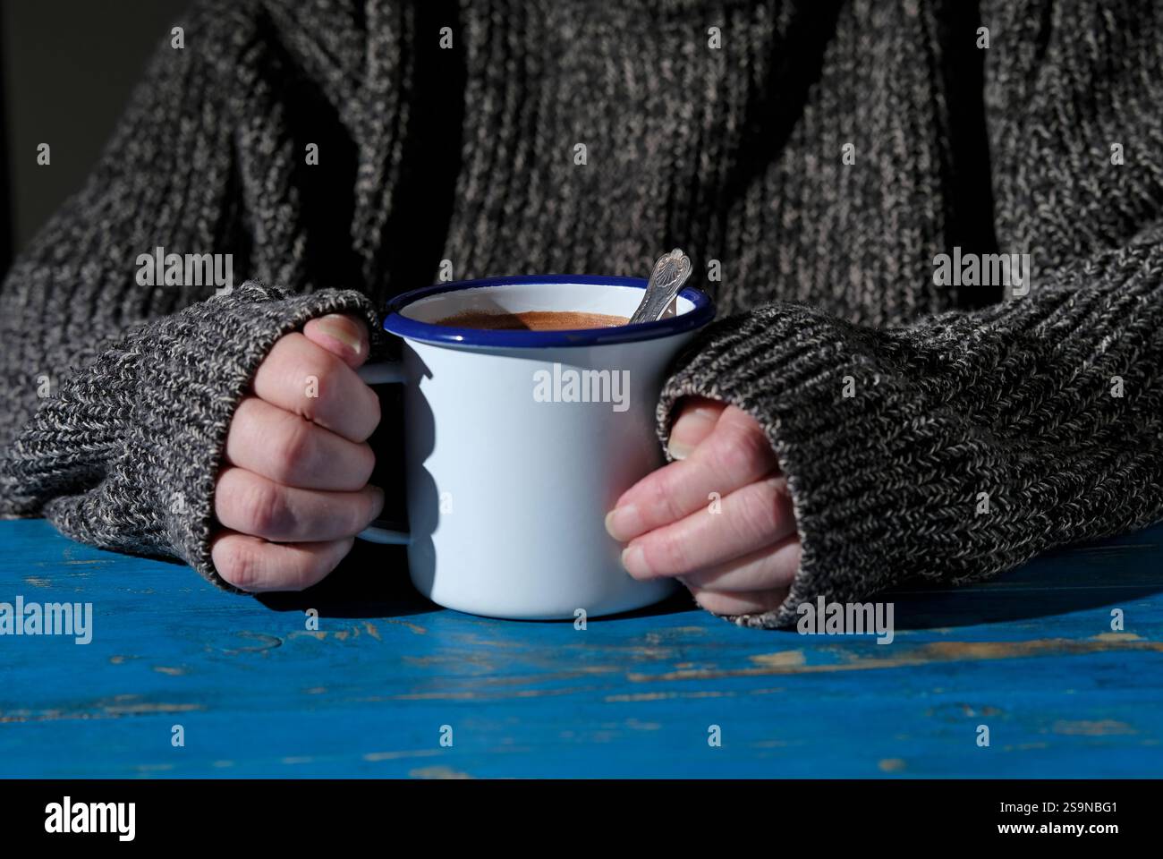 Ältere Frau mit Metallbecher mit heißer Schokolade auf blau lackiertem Tisch Stockfoto