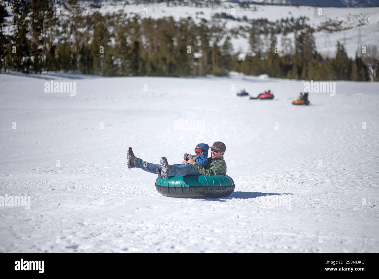 Vater und Sohn Schneeröhre einen Hügel in colorado hinunter. Stockfoto