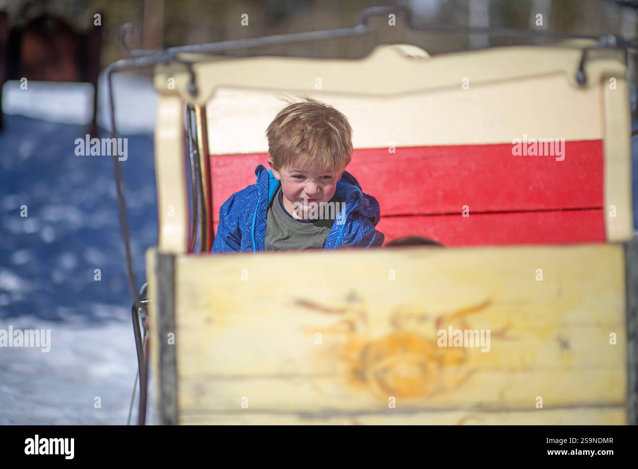 Der kleine Junge hängt in einem hölzernen Schlitten rum Stockfoto