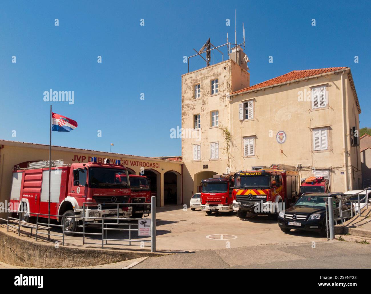 Feuerwehrstation / Feuerwehrstation mit Motoren / Motor und die Feuerwehrfahrzeuge parkten draußen an einem sonnigen Tag mit blauem Himmel / Himmel. Kroatien. (138) Stockfoto