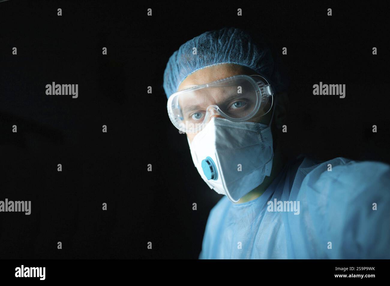Medizinischer Fachmann in Schutzkleidung einschließlich Schutzbrille und Maske, dunkle Einstellung Stockfoto