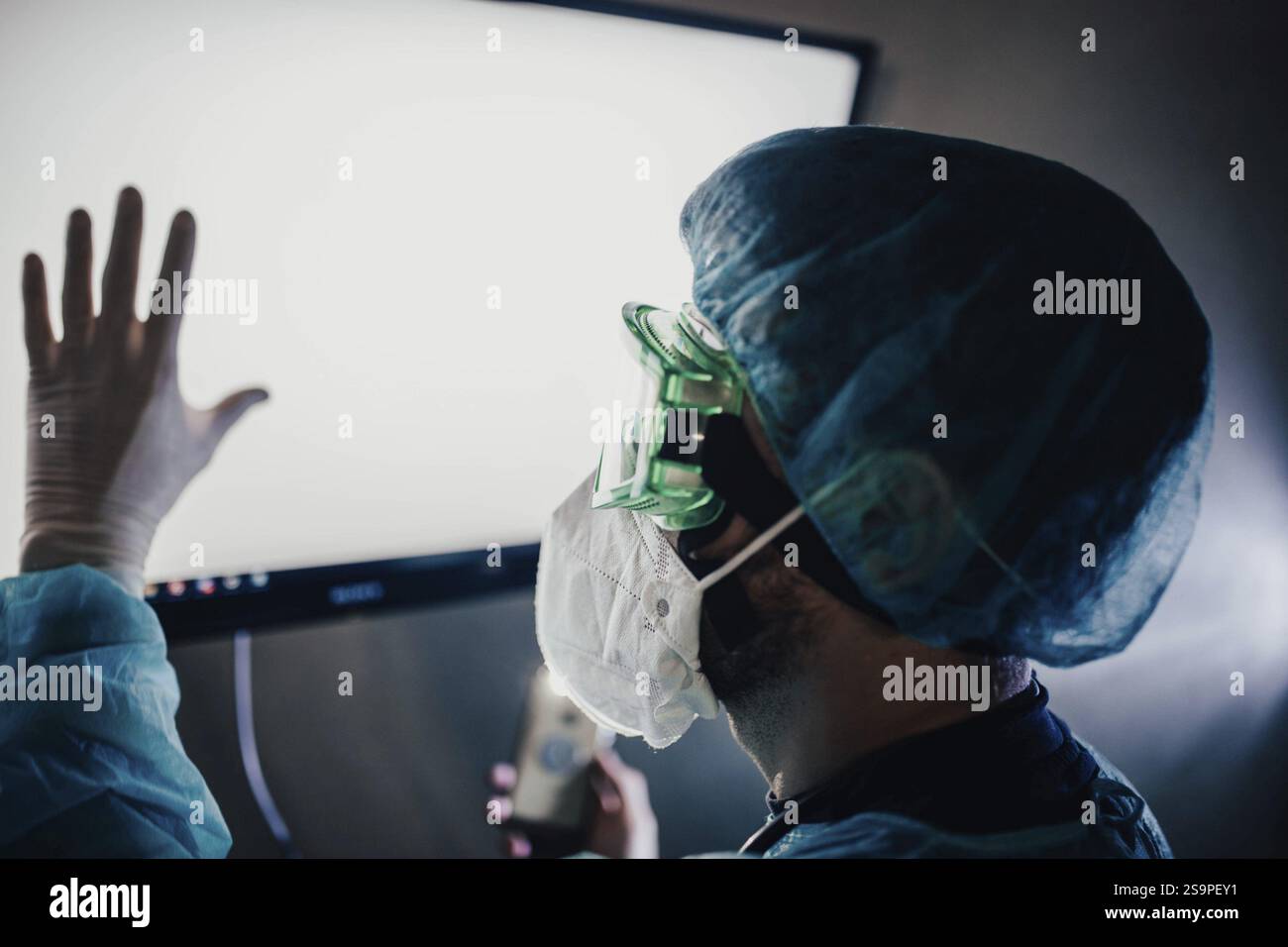 Ein Arzt in Schutzausrüstung, der mit einem hellen Bildschirm interagiert Stockfoto