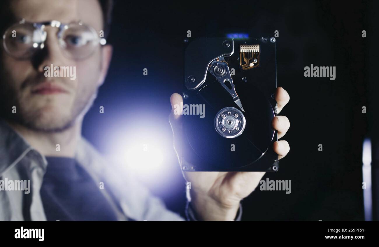 Ein Mann, der eine Festplatte inspiziert, eine Brille trägt, mit einem Fokus auf Technologie und Präzision Stockfoto