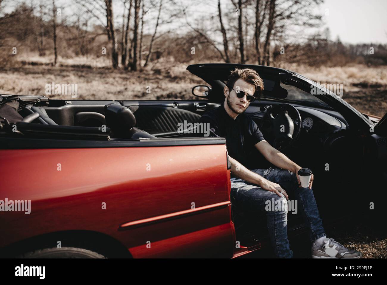 Mann sitzt in einem roten Cabrio, entspannter Ausdruck inmitten eines natürlichen Hintergrunds Stockfoto