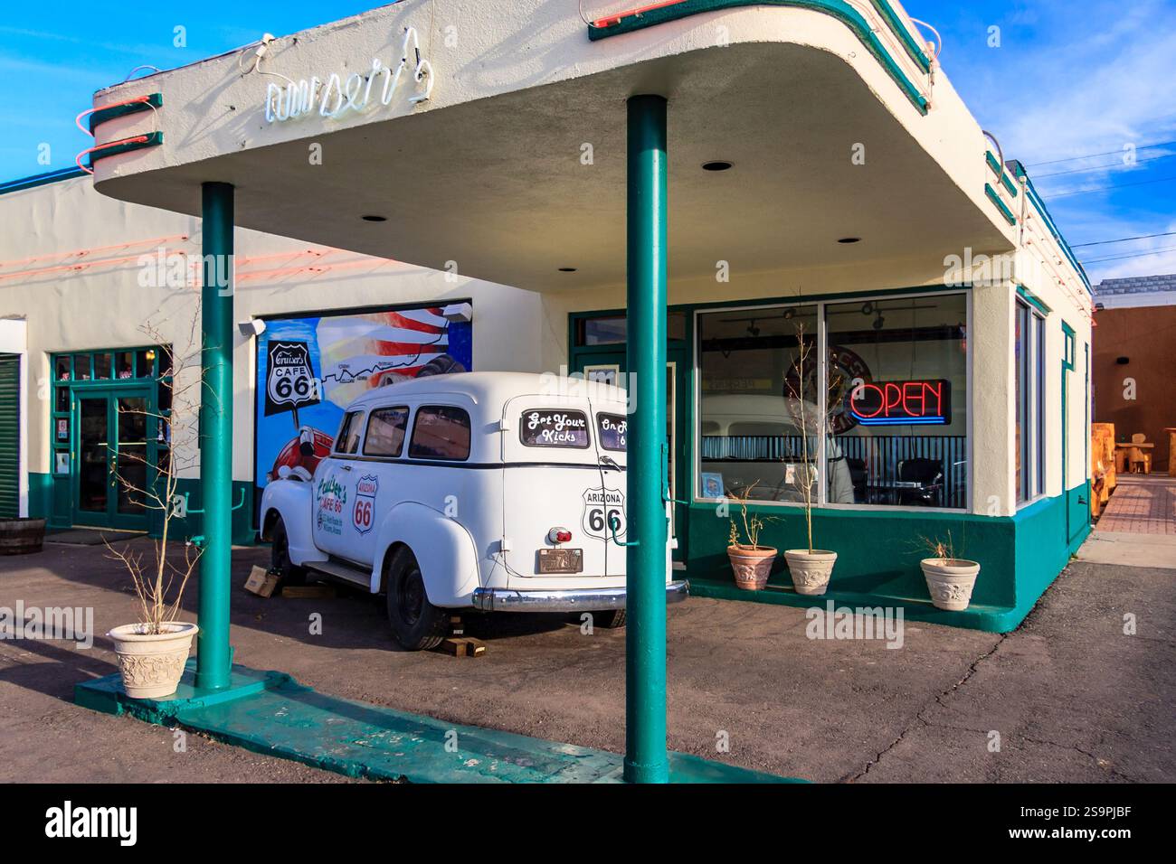 Ein Oldtimer steht vor einer Tankstelle. Die Tankstelle ist offen und hat ein Neonschild mit der Aufschrift „offen“. Das Auto ist alt und hat einen klassischen Look Stockfoto