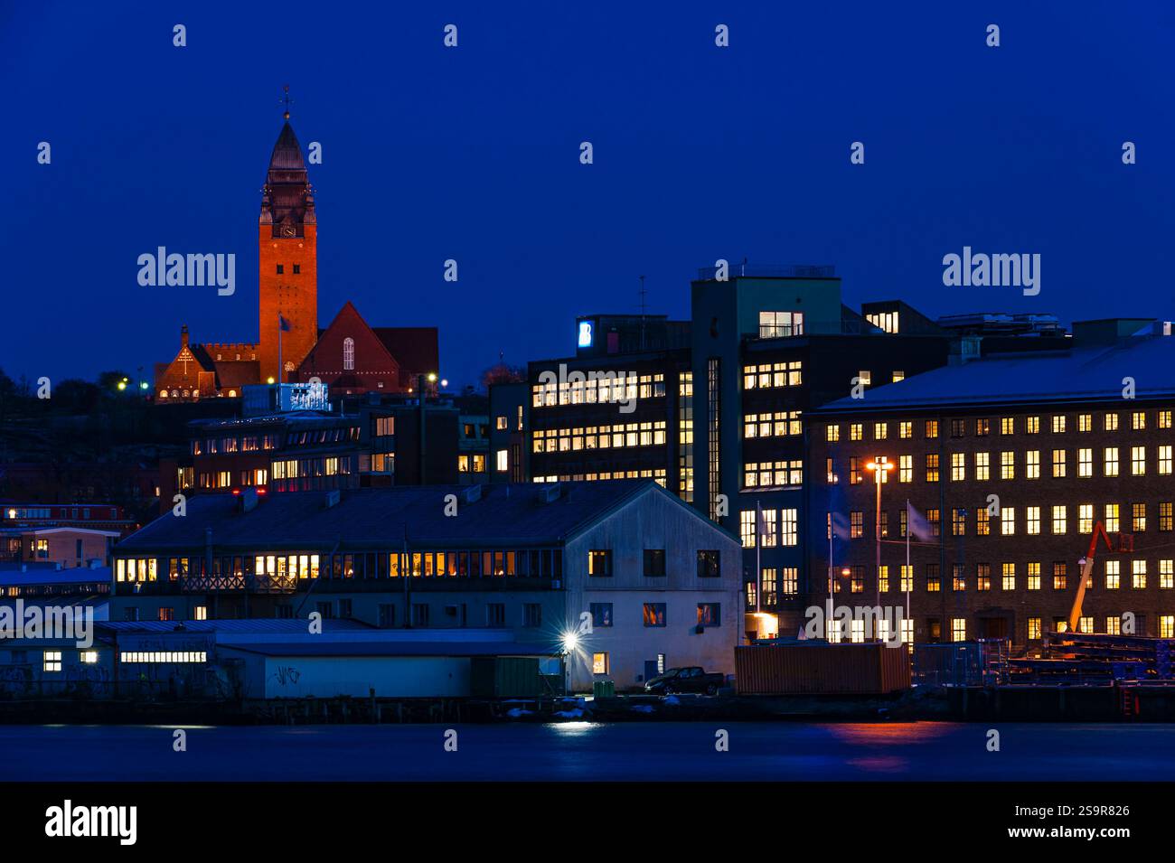 Eine lebhafte Hafenpromenade in Göteborg wird bei Nacht mit beleuchteten Gebäuden und dem markanten Kirchturm zum Leben erweckt. Die Szene fängt das Archi der Stadt ein Stockfoto