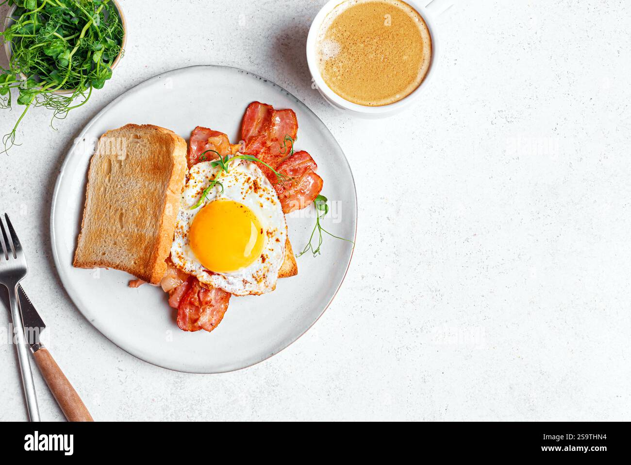 Frühstückssandwich mit Spiegelei, Speck und Kaffee, Blick von oben, Kopierraum. Gebratenes sonniges Ei mit Speck auf Toast mit Mikrogrün und Morning capp Stockfoto