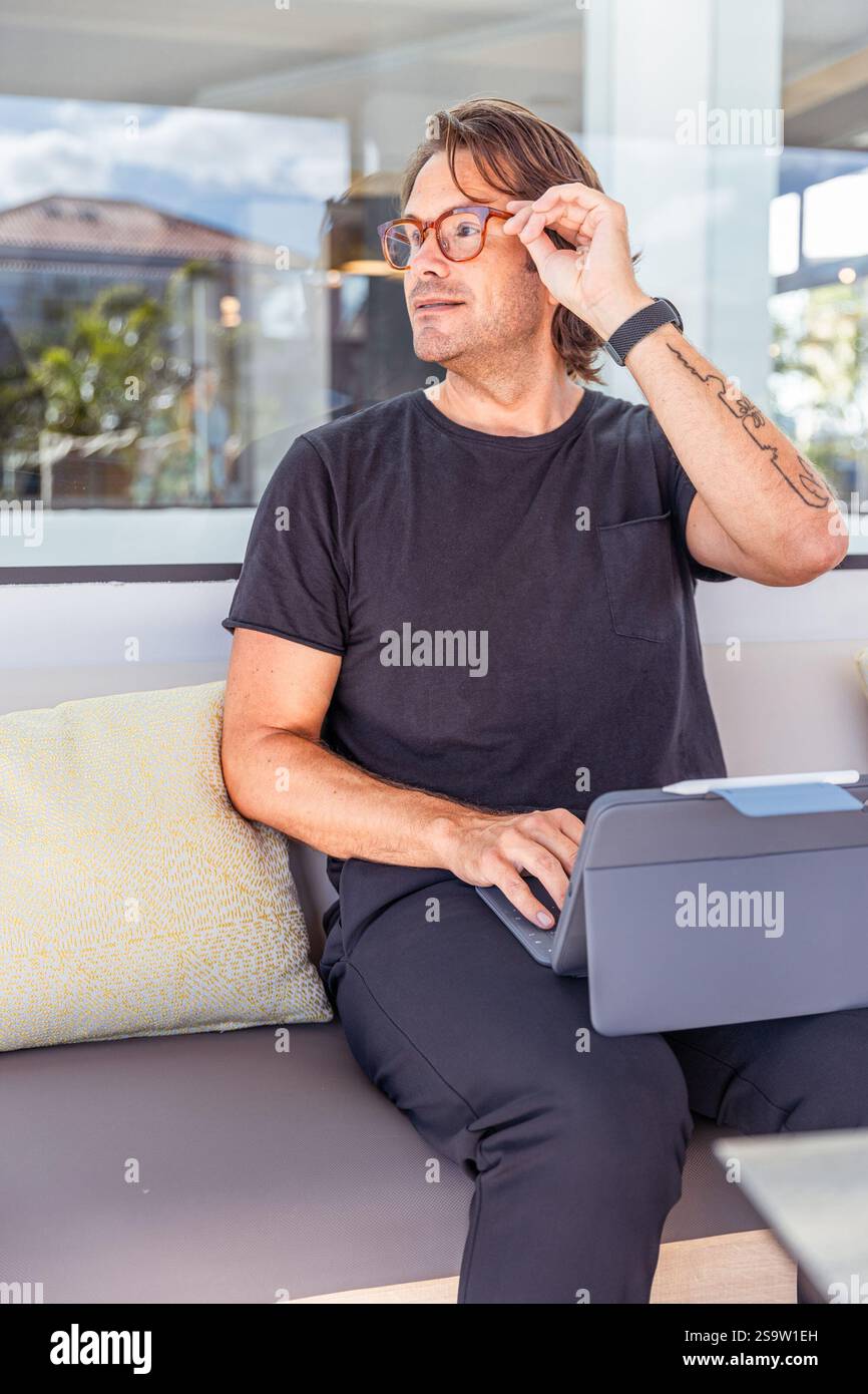 Ein Hipster-Mann in einem schwarzen Hemd berührt seine Brille, während er mit diesem Tablet arbeitet. Produktivitäts- und Konzentrationsbegriff Stockfoto