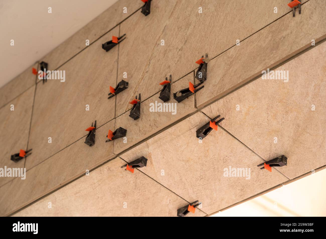 Fliesennivelliersystem mit Kunststoffklammern und Keilen, während der Fliesenmörtel festsitzt. Wandfliesen. Stockfoto