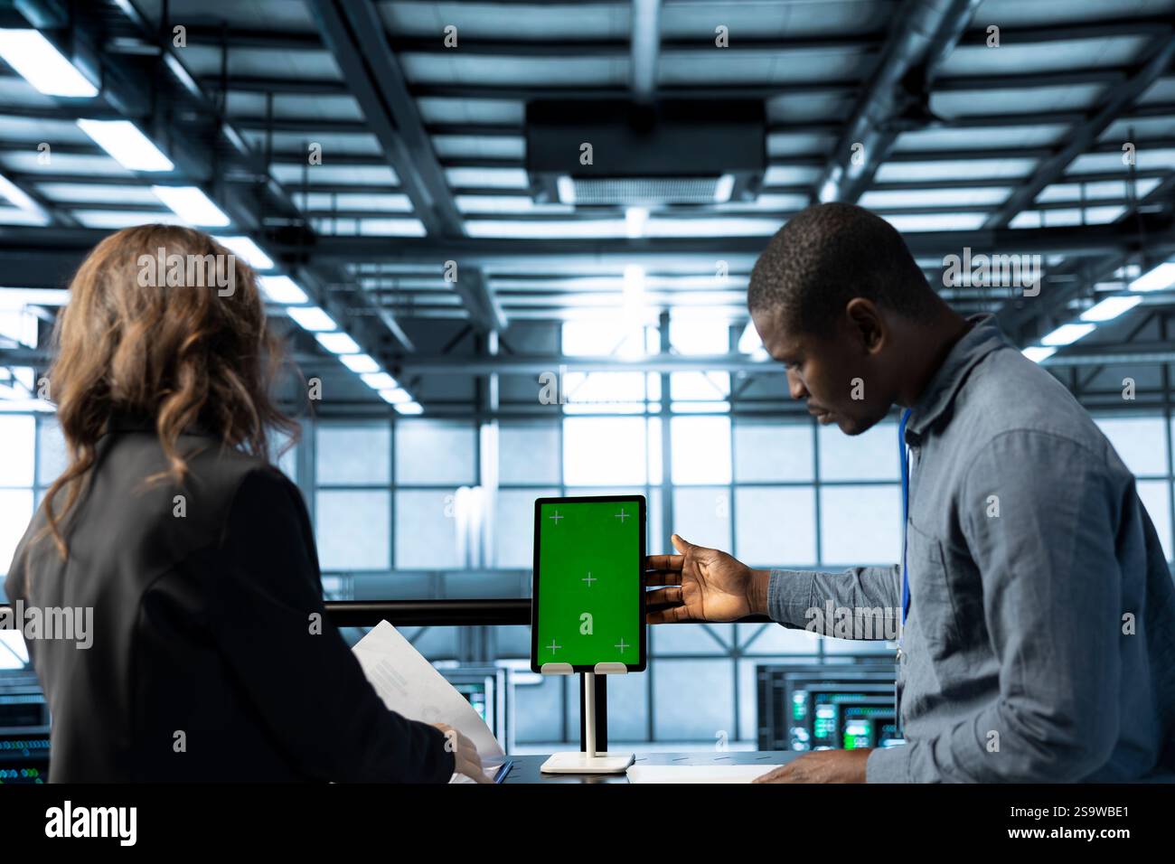 Techniker im Rechenzentrum, die ein Mockup-Tablet mit grünem Bildschirm verwenden, Hardwarediagnosen überprüfen, fehlerzustände löschen, Gerätekonfigurationen anpassen und Firmware-Aktualisierungen anwenden Stockfoto