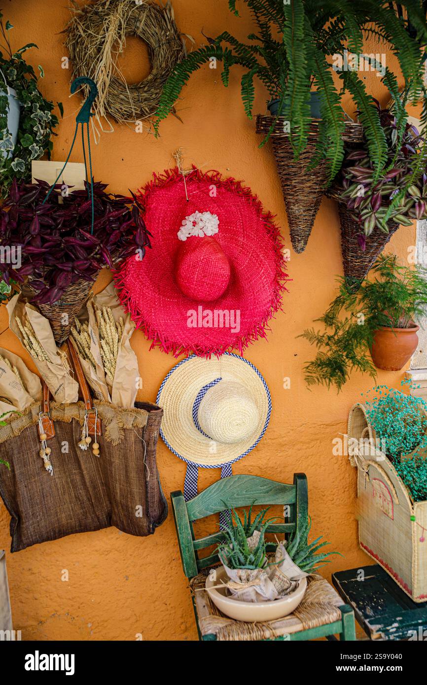 Griechenland. Terrakotta-Wand, hängende Körbe mit Farnen, getrocknete Blumen und Strohhüte Stockfoto