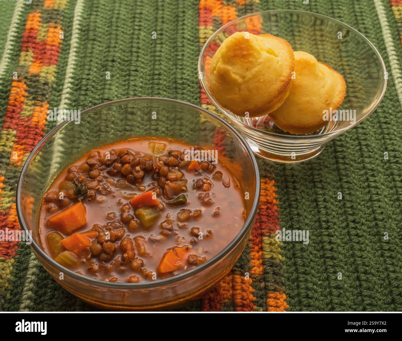 Bunte Linsensuppe mit glutenfreien Maismuffins, serviert in Glasschalen auf einer grünen und rostfarbenen Tischdecke an einem Winterabend; hausgemacht. Stockfoto